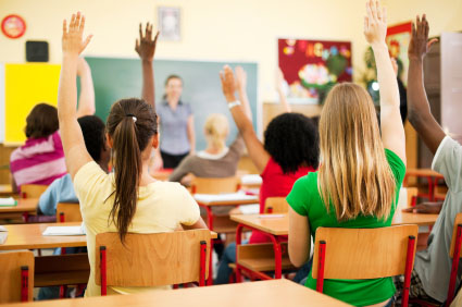 Group of teenagers sitting in classroom with raised hands.